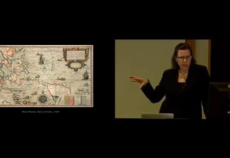 On the right, a white woman in glasses speaks and gestures toward a manuscript map pictured at left. Claudia Swan presenting a talk on Tulips and other Exotics in Golden Age Holland at Krannert Art Museum.