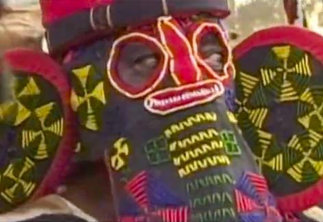 Person in gray elephant head with colored stitching from Bamileke Tso Elephant Masquerade 